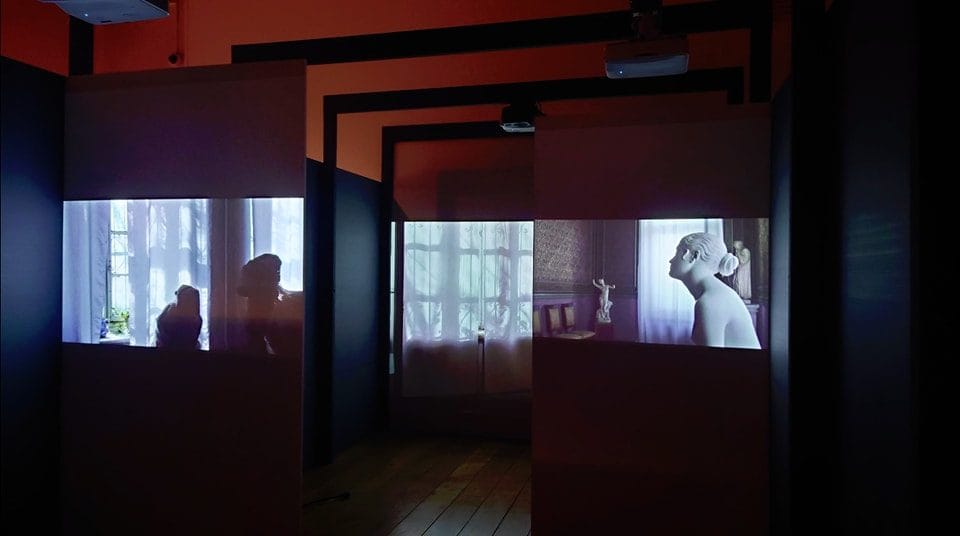 Kunstinstallasjon med video projisert på flere vegger i et mørkt rom