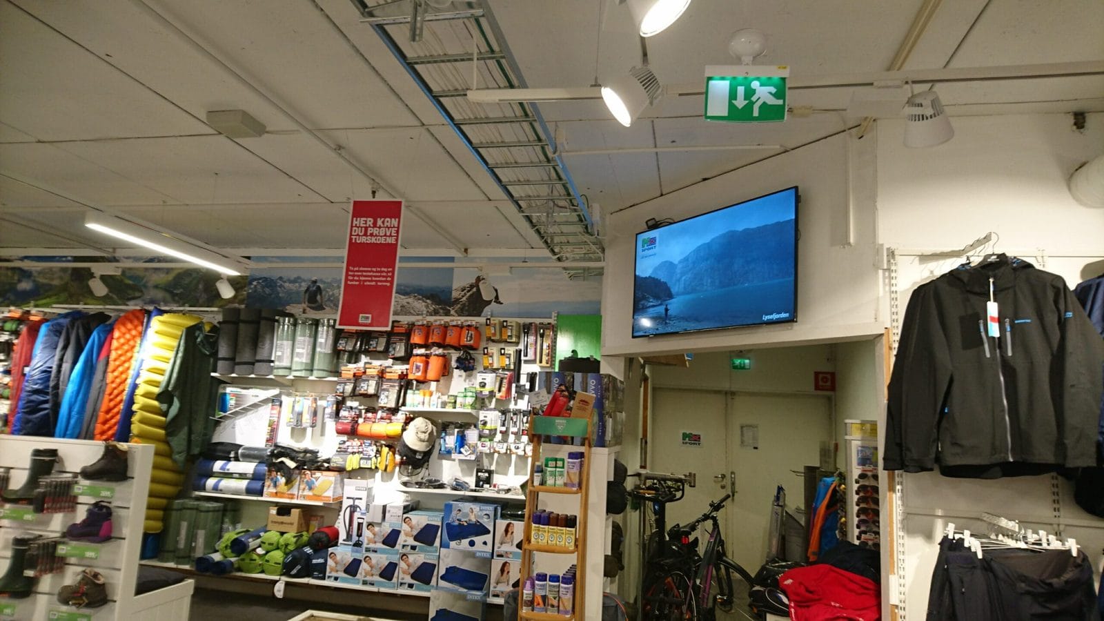 Infoskjerm hengt i taket over hyllene i en sportsbutikk