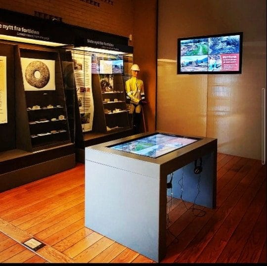 Touchbord med videoknapper i et museumsrom med montre og veggskjerm